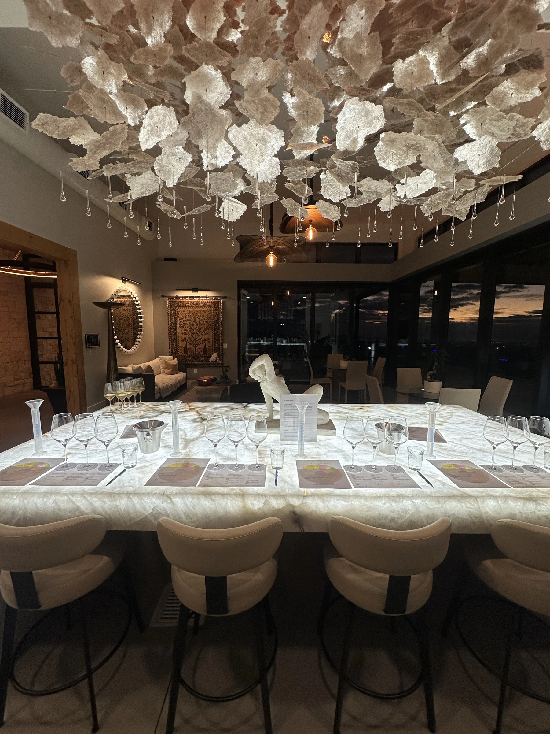 The illuminated tasting table beneath a sculptural chandelier, with views through the glass doors